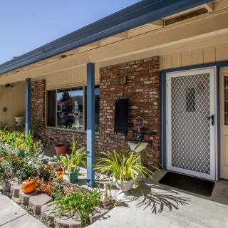 A cozy house exterior with a brick wall, front porch, and a small garden with potted plants.
