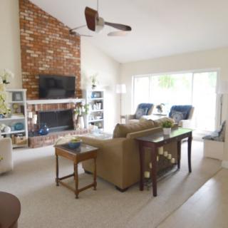 A cozy living room featuring a brick fireplace, comfortable seating, and a large window allowing natural light.