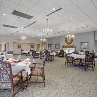 An elegant dining room with neatly arranged tables and chairs, featuring chandeliers and decorative elements.