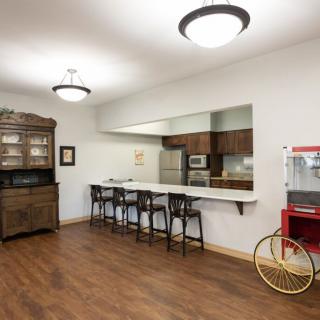 A spacious kitchen area with a counter and bar stools, featuring wooden flooring, a cabinet, and a popcorn machine.