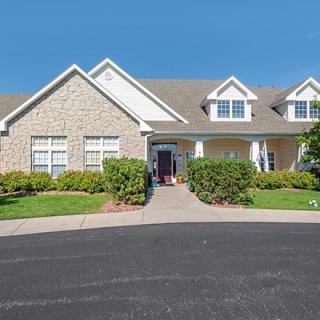 A suburban house with a stone facade, surrounded by well-maintained landscaping under a clear blue sky.