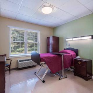 A well-lit patient room featuring a bed, chair, and storage, designed for comfort and care.