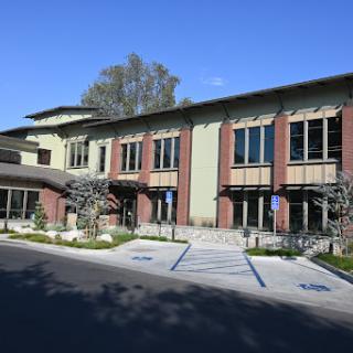 A modern architectural building with a blend of brick and green elements, featuring large windows and a welcoming entrance.