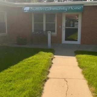Entrance of a small brick building with an awning and a well-maintained lawn.