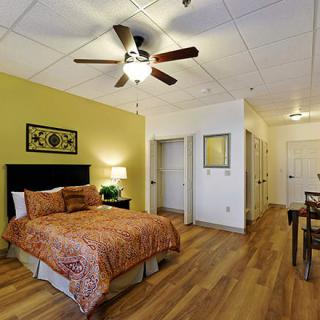 A cozy bedroom with warm-colored decor, featuring a ceiling fan and wooden flooring.
