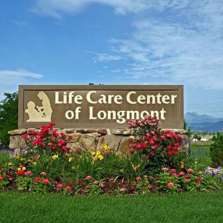 A sign for the Life Care Center of Longmont surrounded by vibrant landscaping and flowers under a blue sky.
