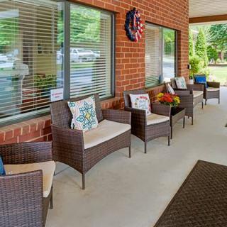 A cozy outdoor patio with wicker chairs and decorative pillows along a brick wall.