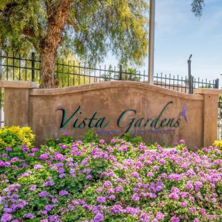 Entrance sign at Vista Gardens surrounded by blooming flowers.