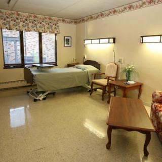 A clean and organized hospital room with a bed, chairs, and large windows allowing natural light.