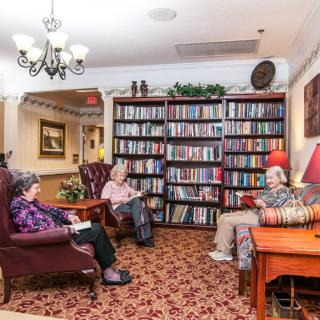 A cozy library with elderly individuals enjoying their reading.
