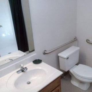 A clean and simple bathroom with a sink, toilet, and mirror, featuring a handrail for accessibility.