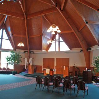 Interior view of a modern church with wooden beams and large windows.