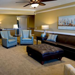 A well-furnished living room featuring a leather sofa, two armchairs, a large ottoman coffee table, and elegant lighting.