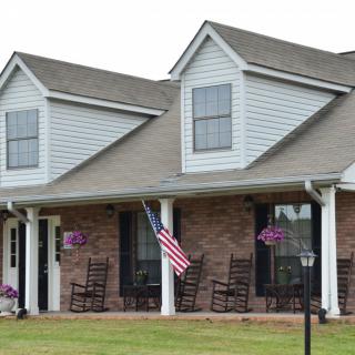 A suburban house with a front porch, displaying an American flag and several rocking chairs.