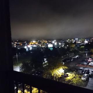 A serene nighttime view of the city from a balcony, illuminated by various lights.