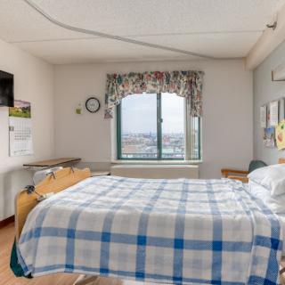 A well-lit hospital room featuring a bed with a checkered blanket and a window offering a view.