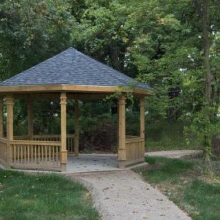A wooden gazebo surrounded by trees with a pathway leading to it.