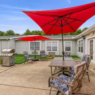 A cozy backyard patio with red umbrellas, a grill, and outdoor seating on a sunny day.