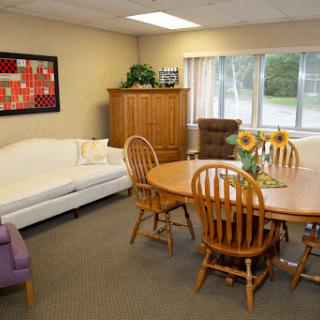 A cozy living and dining area featuring a white sofa, wooden dining table with chairs, and decorative sunflowers.