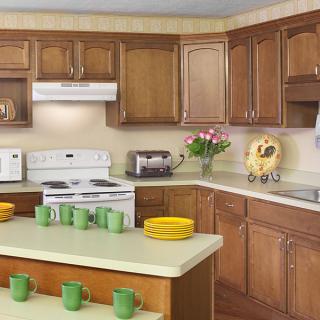 A cozy kitchen featuring wooden cabinets, a white stove and microwave, and colorful dishware on the countertop.