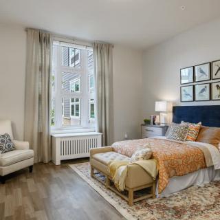 A modern, cozy bedroom with ample natural light, featuring elegant decor and a large window.