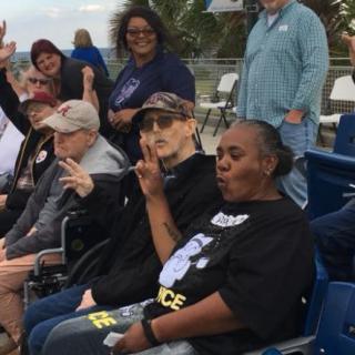 A group of people seated outdoors, some in wheelchairs, making peace signs.