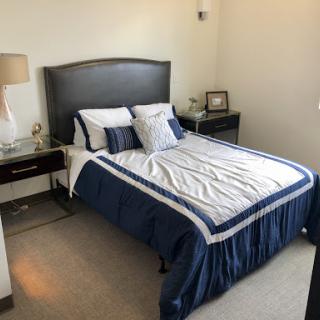 A cozy bedroom featuring a neatly made bed with blue and white bedding, accompanied by a stylish nightstand and lamp.