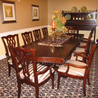 A well-decorated dining room featuring a large wooden table surrounded by chairs, with elegant decor and warm lighting.