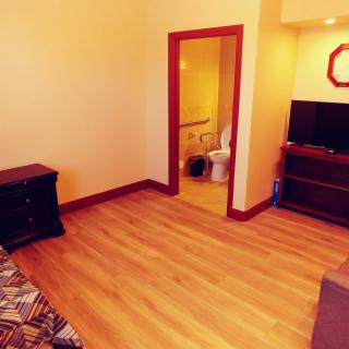 A cozy bedroom with wooden flooring, featuring a television and an open doorway leading to a bathroom.