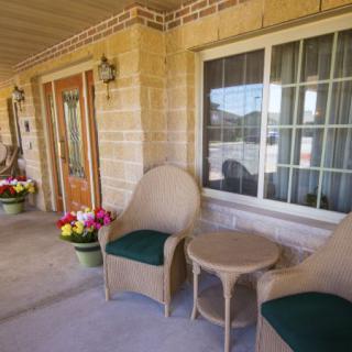 A cozy porch area with two chairs, a small table, and colorful flowers by the front door.