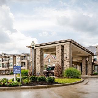 A modern building entrance with well-maintained landscaping and a cloudy sky backdrop.