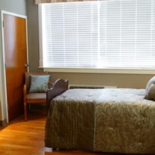 A cozy bedroom with a bed, chair, and large window with blinds.