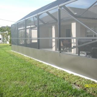 A screened-in outdoor patio with a surrounding lawn on a sunny day.
