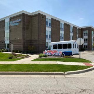 A healthcare facility with a bus parked in front, showcasing the outdoor landscaping.