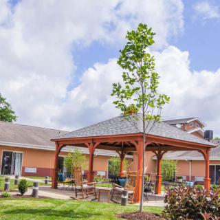 A scenic outdoor area featuring a wooden gazebo and garden under a partly cloudy sky.