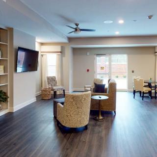 A modern living room with comfortable seating and a television, featuring wood flooring and bright windows.