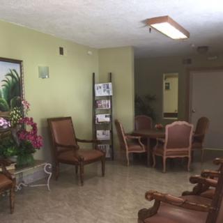 An indoor waiting room featuring a seating area with chairs, a table, and decorative plants.