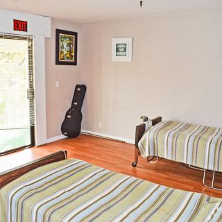 A minimalist bedroom with two beds and a guitar case by the window.