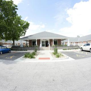 A well-maintained building with a clear blue sky, surrounded by greenery and parked cars.