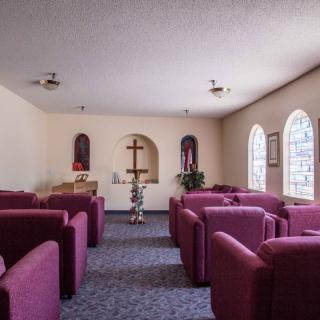 A small chapel with rows of upholstered seating facing a cross on the wall.