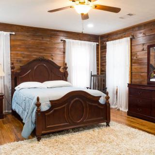 A cozy bedroom with wooden walls, featuring a large bed, ceiling fan, and natural lighting.
