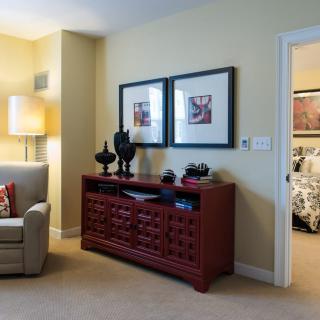 A cozy living room with a comfortable armchair, decorative artwork above a wooden cabinet, and a soft glowing lamp.