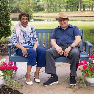 A couple sitting on a bench surrounded by flowers in a park.