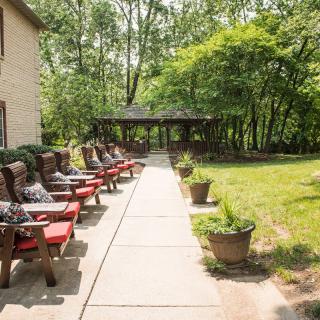 A peaceful outdoor patio area with rows of chairs and a pathway leading to a gazebo surrounded by lush greenery.