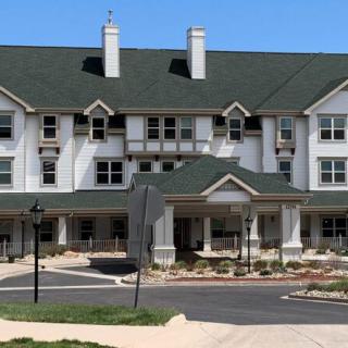 A large three-story residential building with green roofs and landscaped surroundings on a sunny day.