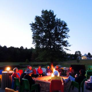 A group of people gathered around a campfire in an outdoor setting during the evening.