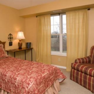 A cozy bedroom with a single bed, warm lighting, and striped chair.