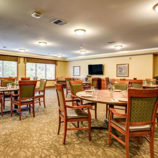 A spacious dining room with neatly arranged tables and chairs, featuring a warm interior design with large windows and ceiling lights.