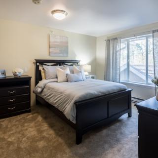 A cozy bedroom with a large bed, dresser, and natural light from a window.
