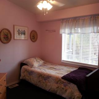 A cozy bedroom with pink walls, featuring a single bed by the window and decorative wall hangings.